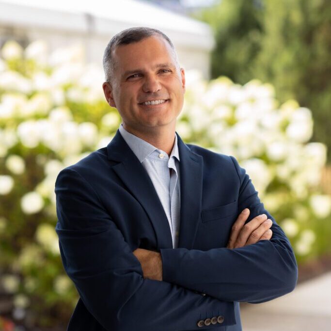 2024_GTS_DanAylward_MAS_1472_HighRes-683x1024 Smiling man in suit, arms crossed.