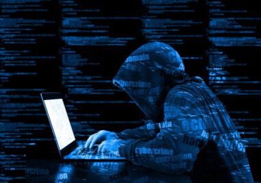A person in a black hoodie is on his laptop.